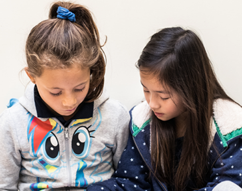 Two young girls are reading a bilingual book