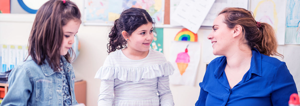 A teacher's speaking with two young students in a classroom